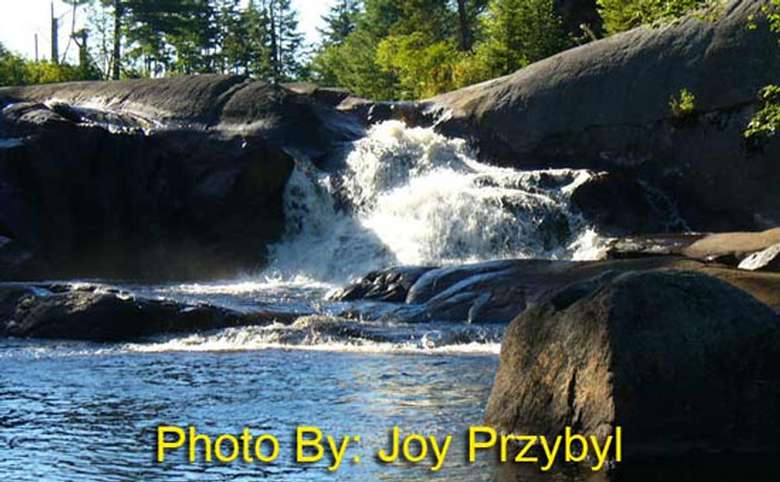 waterfall rushing over a large rock with photo credit to joy przybyl