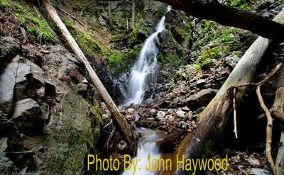 narrow waterfall dropping down rocks in the woods with photo credit to john haywood