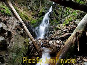 narrow waterfall dropping down rocks in the woods with photo credit to john haywood