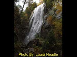 large waterfall dropping through the woods in the fall with photo credit to laura neadle