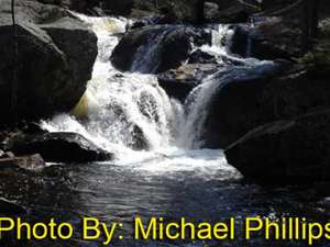 small waterfall flowing around and over rocks with photo credit to michael phillips