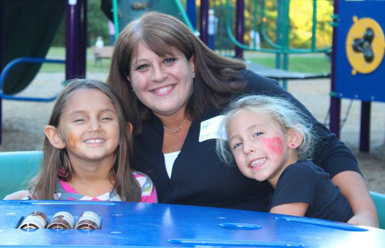 A woman and two children smiling on a playground