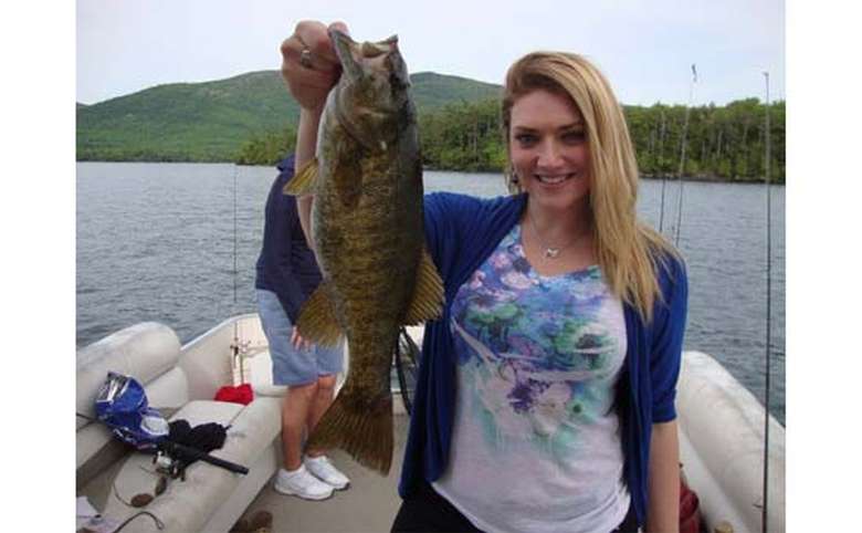 Woman holding up a large bass on a boat in Lake George