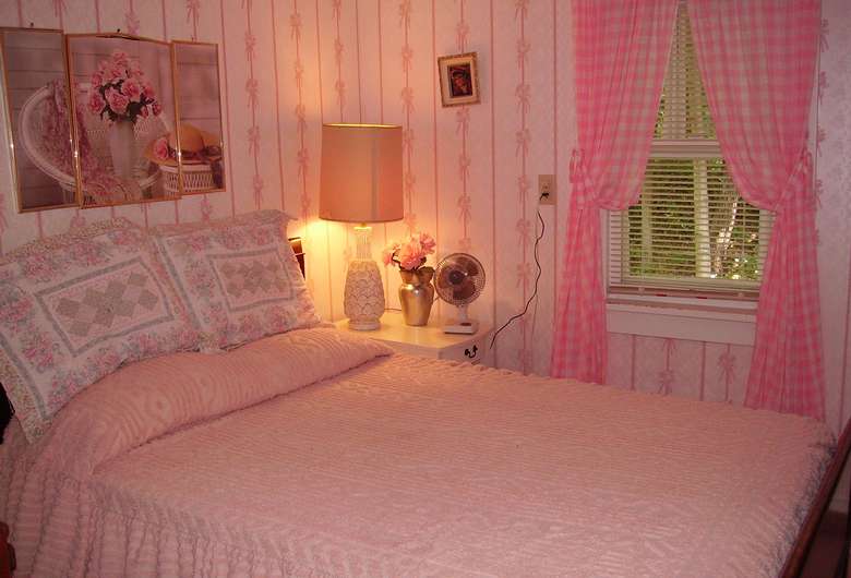 a pink themed bedroom with a bed, a lamp, and a small fan