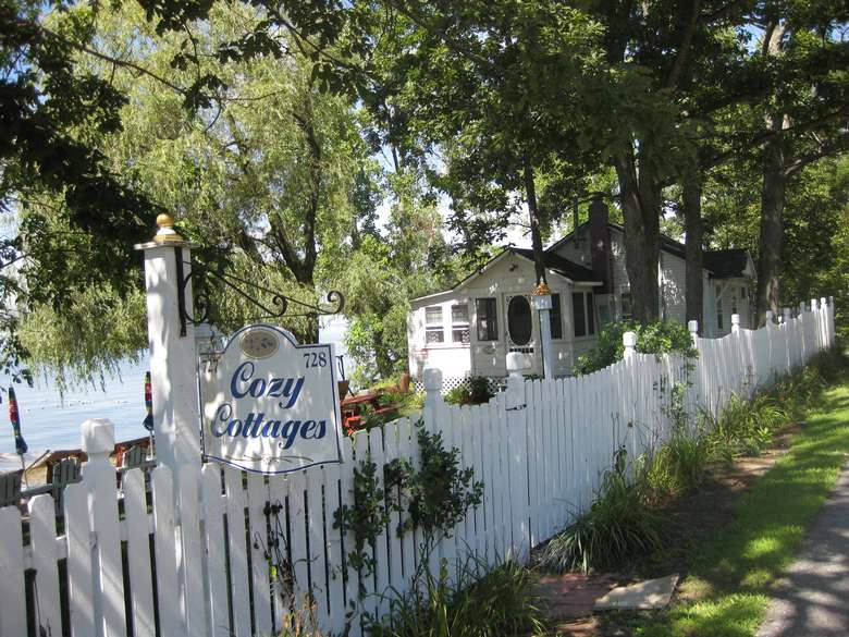 a white fence near a cottage with a sign that reads Cozy Cottages