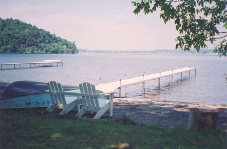 a long dock extending out from a sandy beach with adirondack chairs on it
