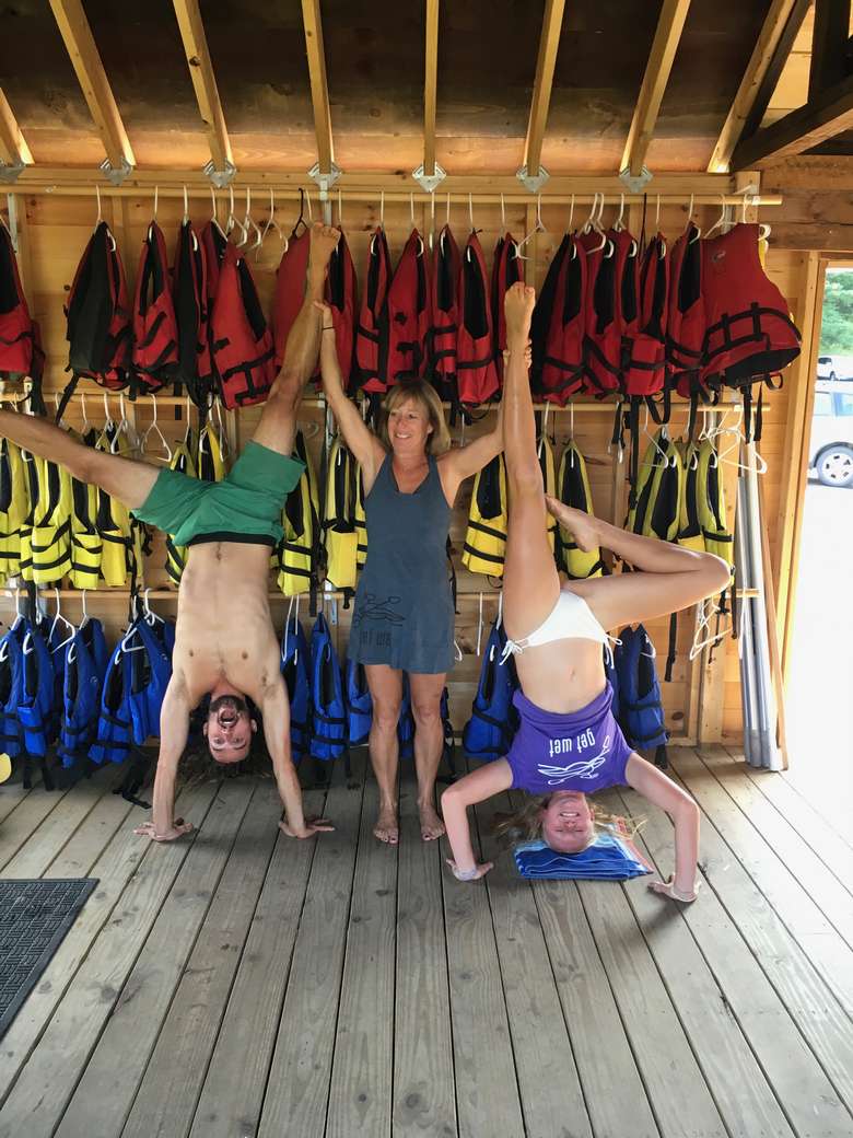 woman holding the legs of two other people who are posing upside-down with racks of life jackets in the background