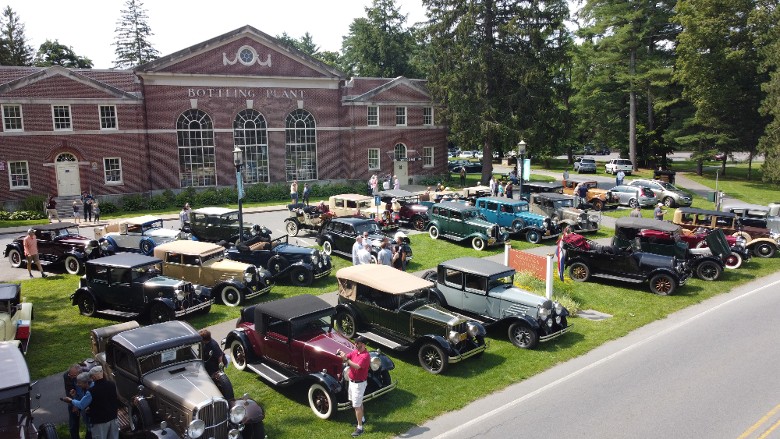 a drone shot of a car show in front of a museum