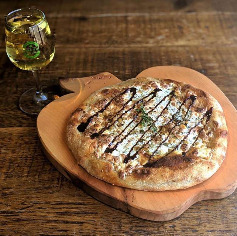 A flatbread pizza and a glass of cider placed on an apple shaped wooden board