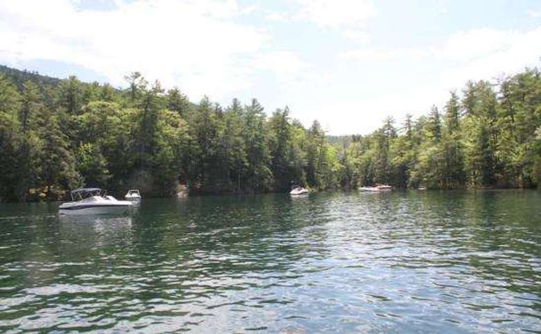 a boat in the water with some rocks in the background near a shoreline