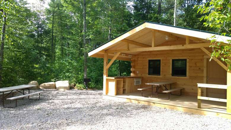 a wooden cabin with an overhanging roof and green trees behind it