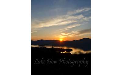 a bright sunrise shining over a lake and mountain