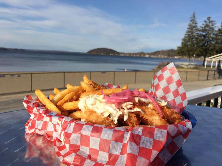 a plate of fries and breaded fish on a table by the lake