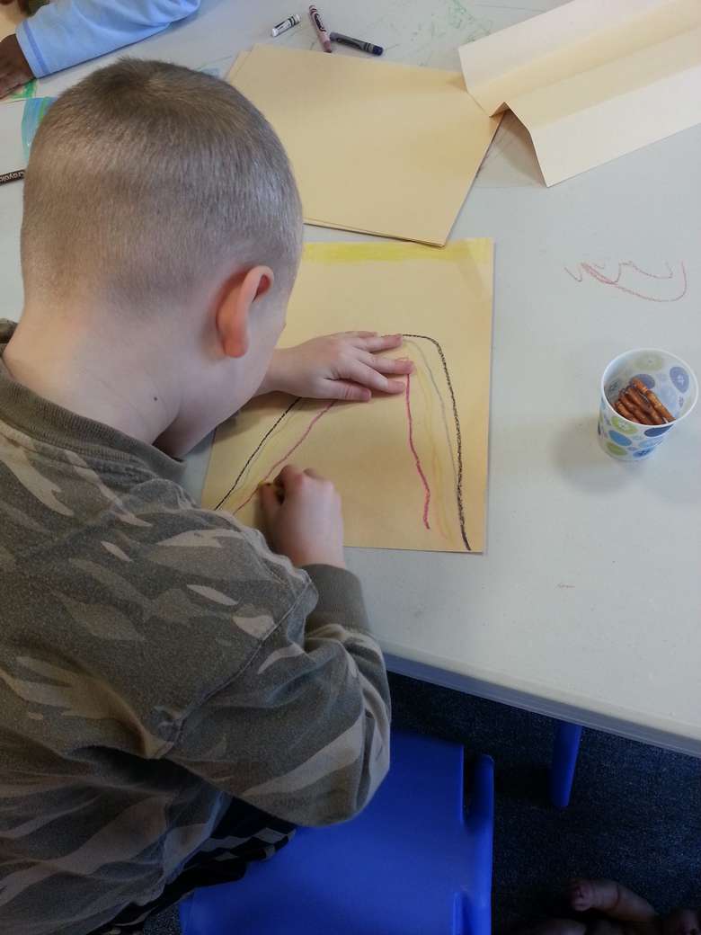 boy in an army patterned shirt drawing a rainbow