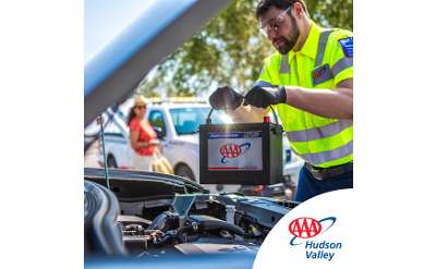 Image of male Triple A Fleet Driver replacing member's vehicle battery with a premium Triple A batter, member smiling as she looks on in background