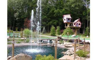 mini-golf course with a water feature in the middle and whimsical looking treehouses in the background