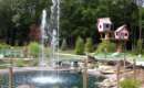 mini-golf course with a water feature in the middle and whimsical looking treehouses in the background