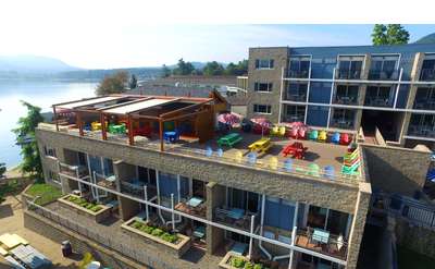 view of a rooftop deck with colorful tables and chairs from the water with hotel rooms behind it