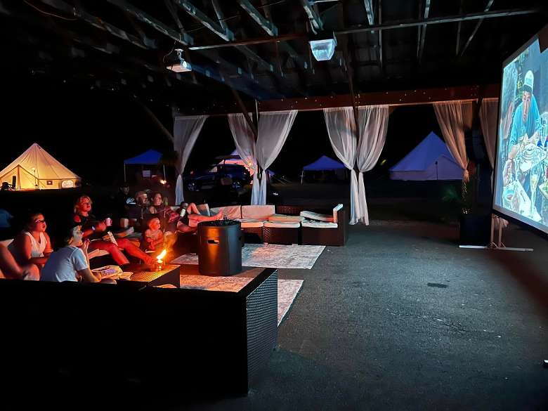 people sitting in an outdoor covered lounge and watching a movie at night