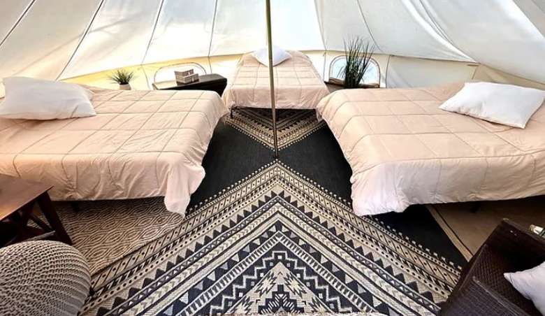 three queen size beds and rugs in a glamping tent