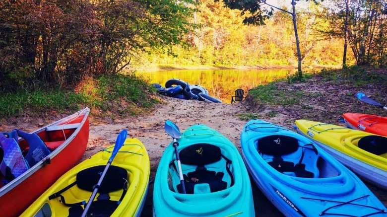 row of colorful kayaks by a sandy path to a river
