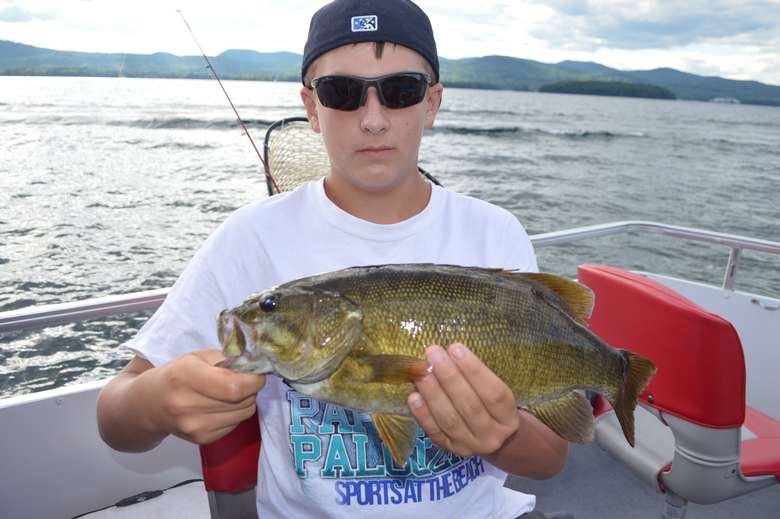 A young man in sunglasses and a backwards hat holding a bass