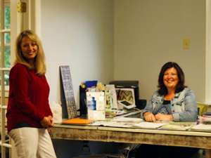 one woman sitting at a desk while another woman stands near it