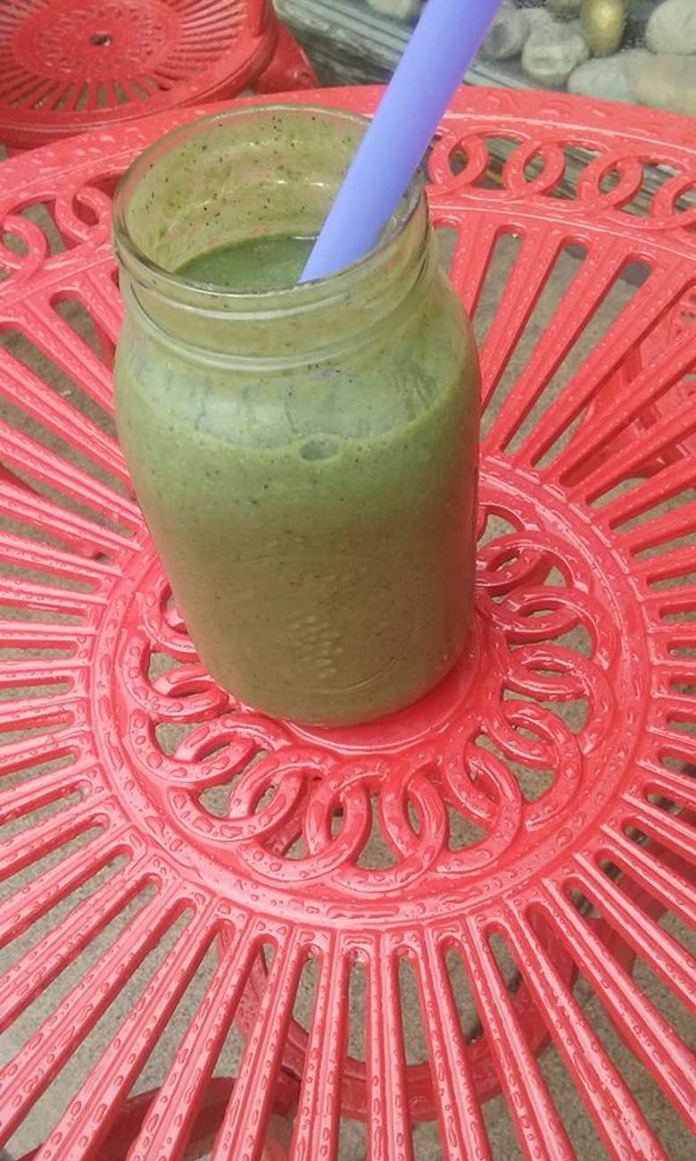 green smoothie in a mason jar with a purple straw on a pink table