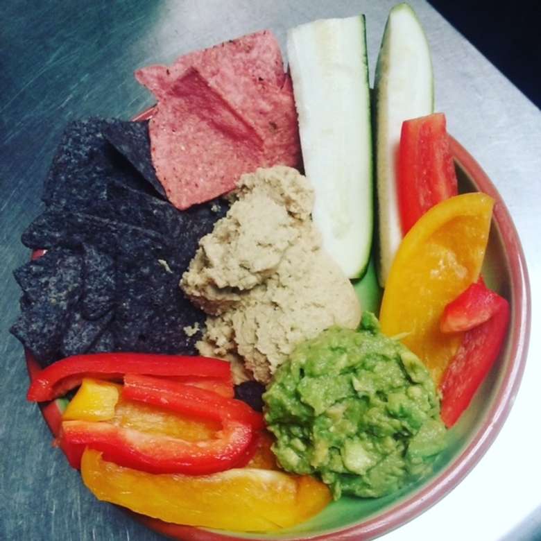 bowl with hummus, guacamole, sliced bell peppers, and blue corn chips