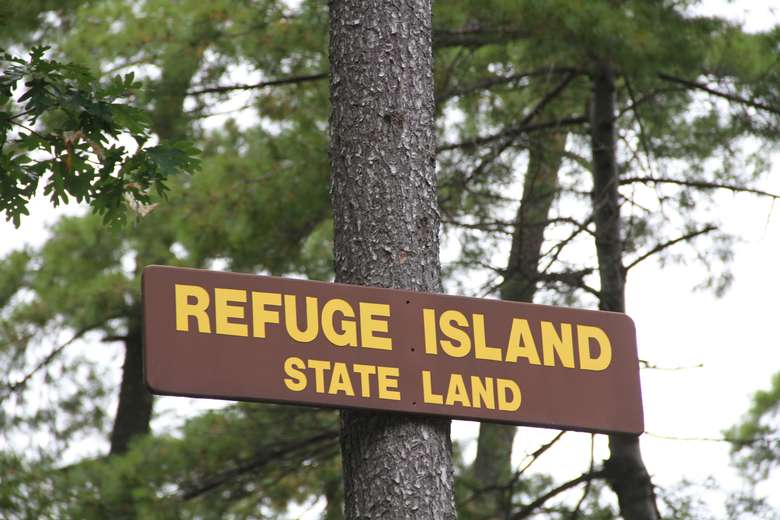 the sign for refuge island state land attached to a tree