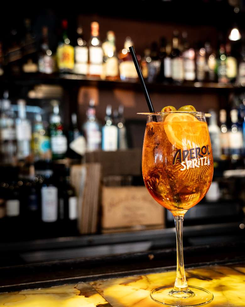 Aperol spritz with an orange and olive garnish on a bar top