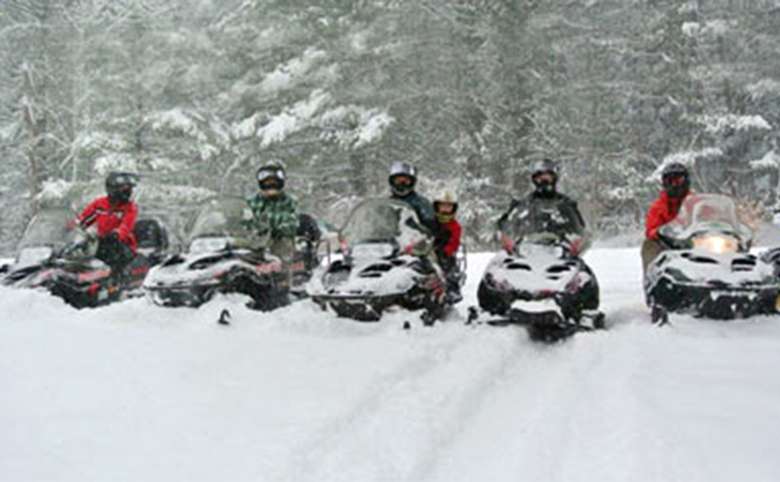 Snowmobiles lined up in the forest with people on them