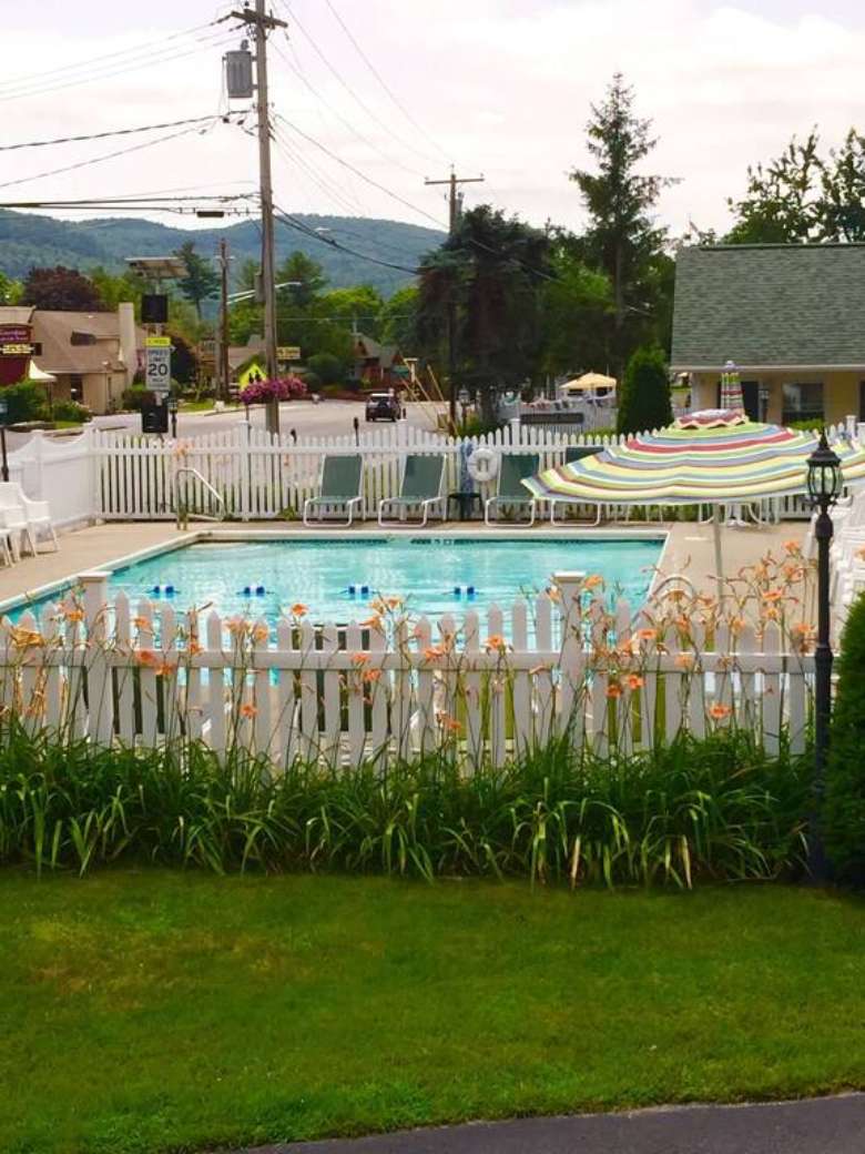 Outdoor in-ground pool surrounded by patio furniture, including chairs, lounge chairs, and a dining table with umbrella.
