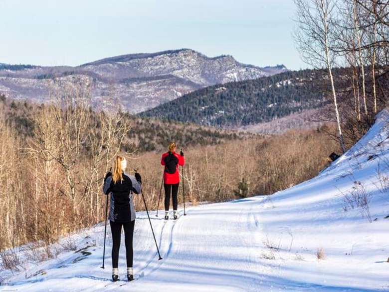 two women cross country skiing along a path in the woods