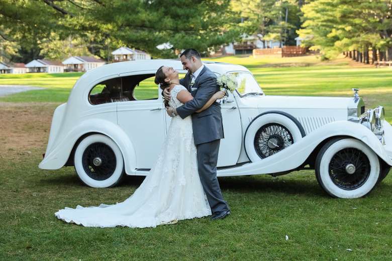 bride and groom embrace in front of old fashioned car