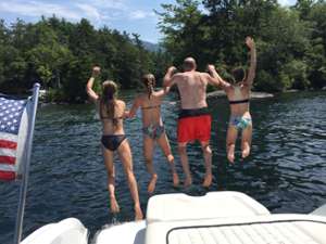 four people holding hands and jumping off a boat into the water
