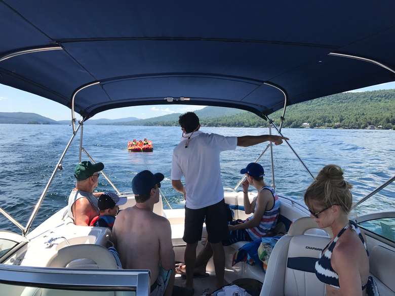 group of people in a boat watching a tube be pulled behind