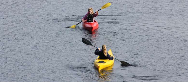 two girls paddling red and yellow kayaks