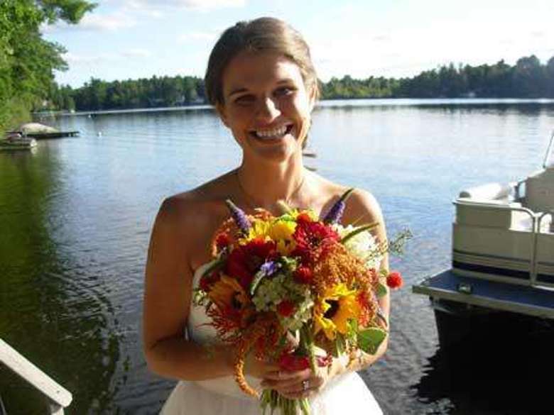 bride smiling and holding a colorful bouquet with a lake in the background