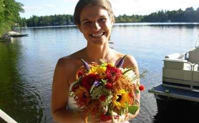 bride smiling and holding a colorful bouquet with a lake in the background