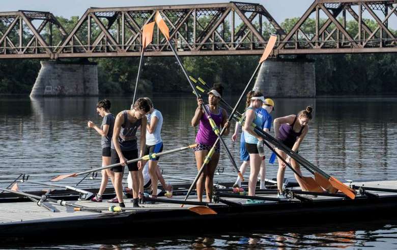 Large group of people holding oars by a bridge
