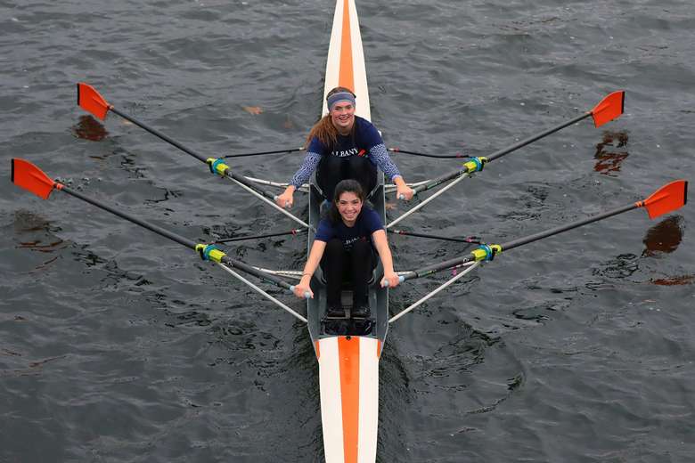 Two girls looking up at the camera smiling while rowing