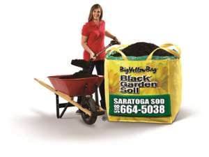 woman shoveling soil from a red wheelbarrow into a big yellow bag