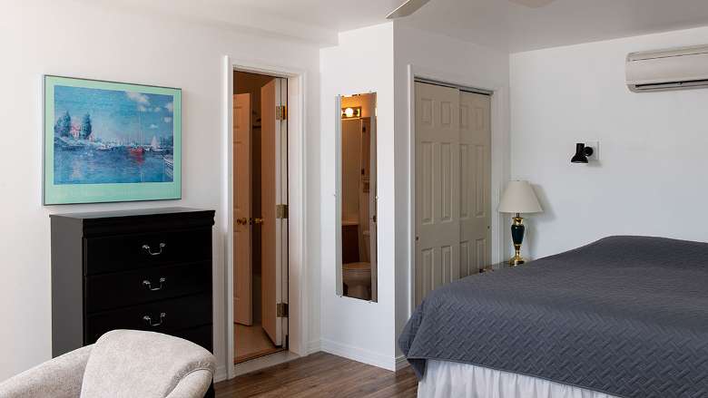 a bedroom with a painting of a lake, a dresser, and a bed with dark blue covers
