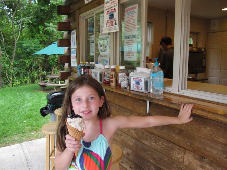 a little girl poses in front of the snack stand with an ice cream cone