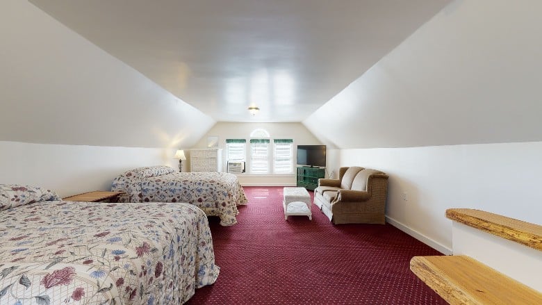 a bedroom with two beds, a sofa, tv and light streaming in the window