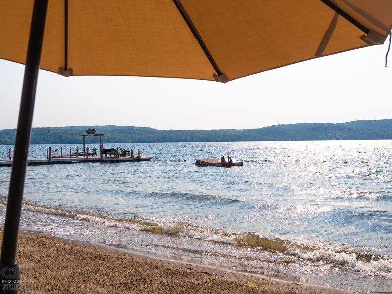 Photo from under a beach umbrella looking at a floating raft and a dock