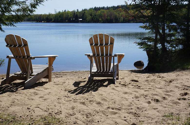 two Adirondack chairs on a beach facing the water