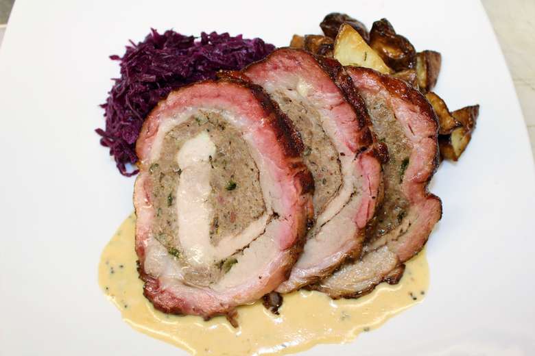 a stuffed pork roll served atop a sauce and potatoes