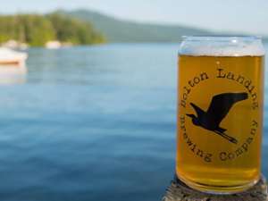 a glass of beer on a dock with the bolton landing brewing company logo on it